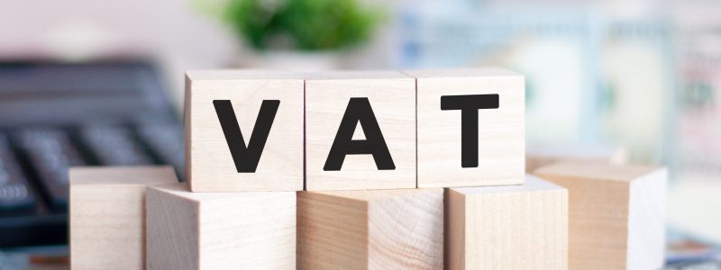 The word VAT on wood cubes, banknotes and calculator on the background. VAT - short for Value Added Tax. Business and finance concept.